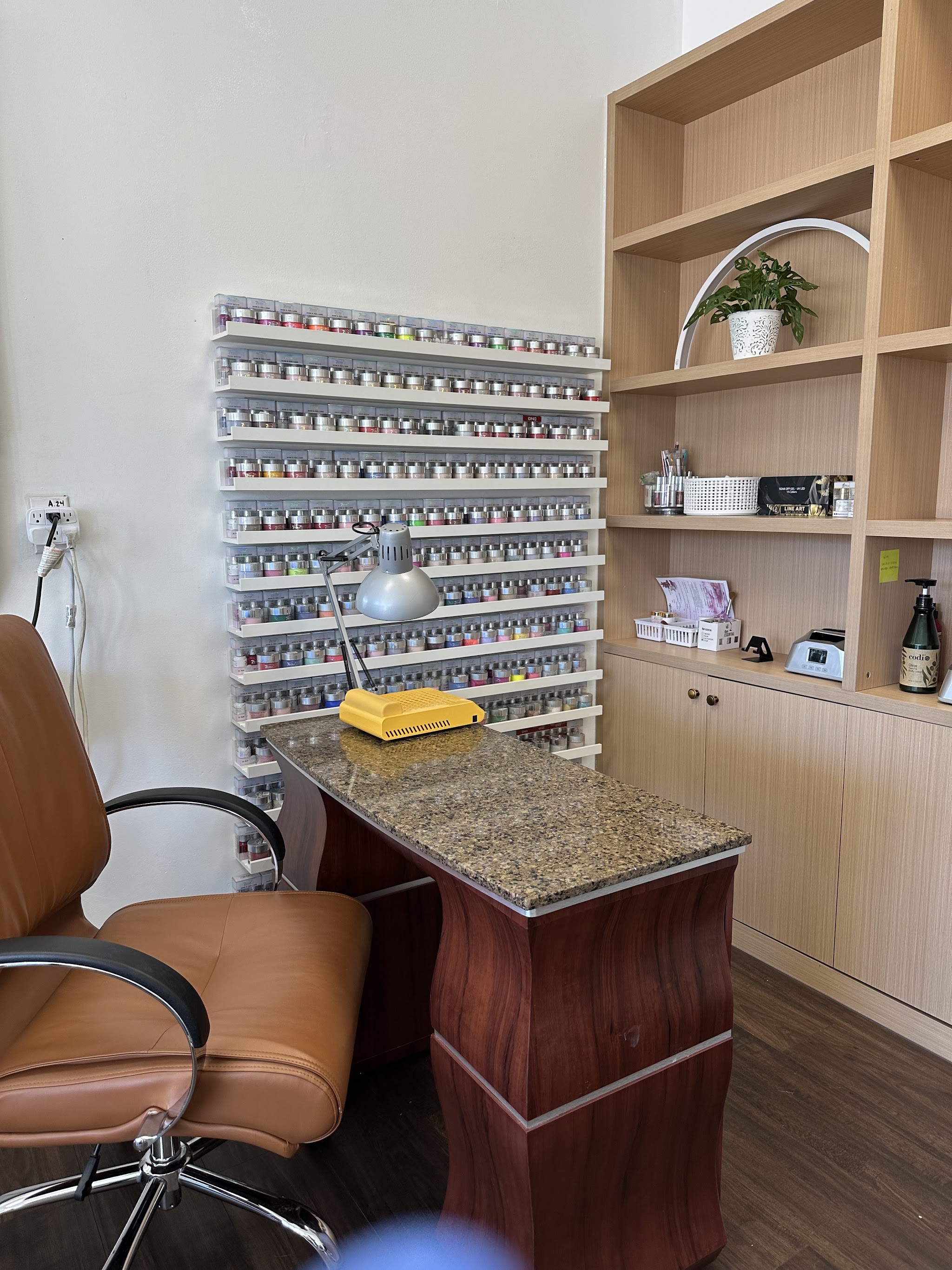 A manicure station in front of a wall of nail colour jars, with a tan leather chair
