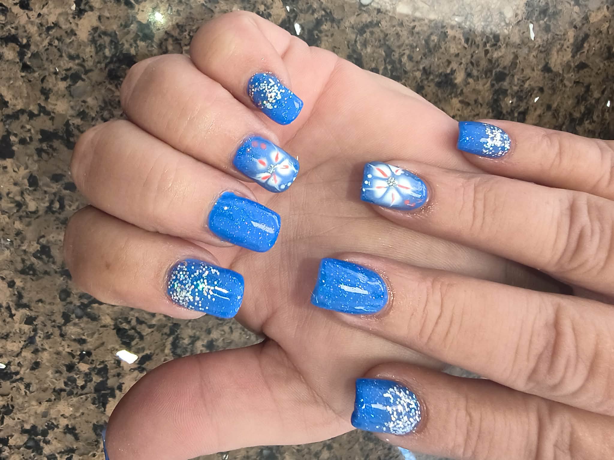 Bright blue nails with glitter fades and white flower accents